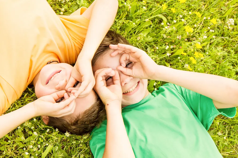 Young children laying in grass making circles around their eyes