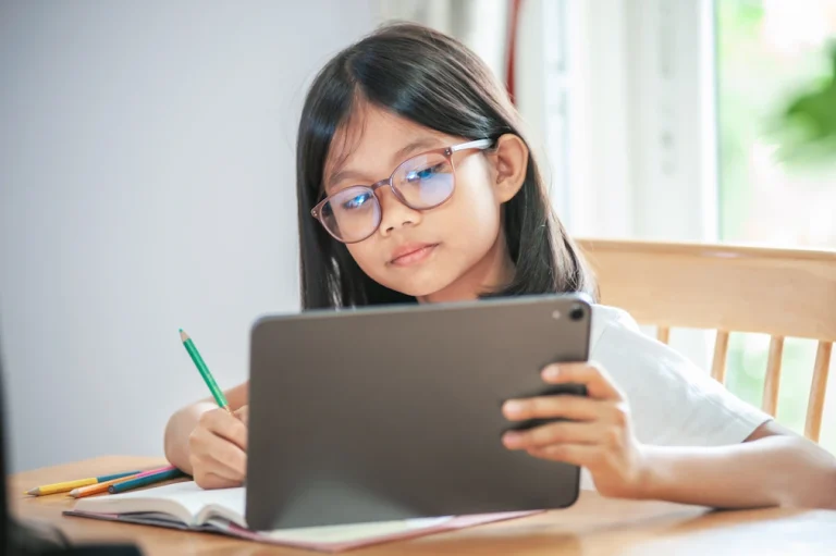 Young girl with glasses learning on tablet and writing
